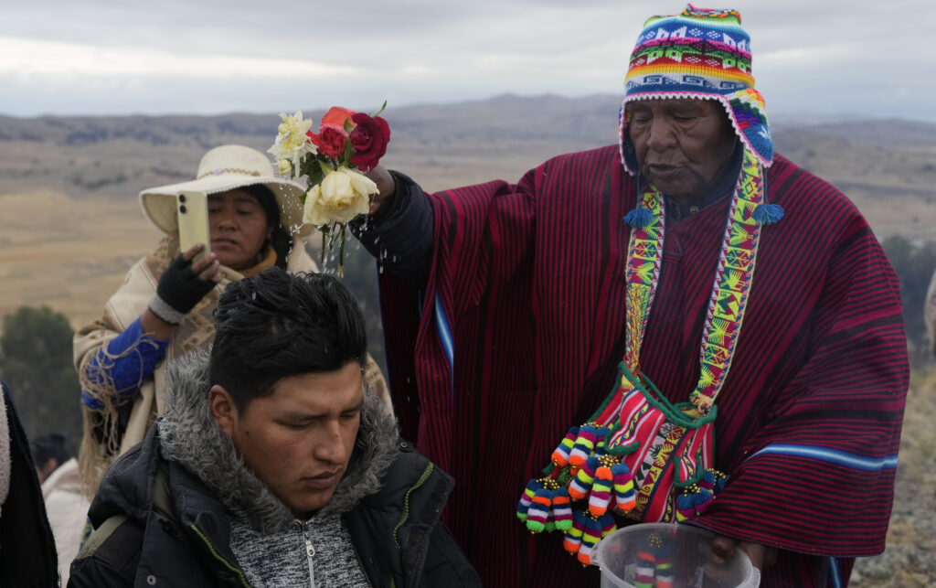 Spiritual leader Jose Mamani blesses a person with water during a New Year's ritual after receiving the first rays of sunlight on Turriturrini Mountain on the outskirts of Huarina, Bolivia, Friday, June 21, 2024. Aymara Indigenous communities are celebrating the Andean New Year 5,532 or "Willka Kuti" which translates to "Return of the sun" in Aymara. (AP Photo/Juan Karita)