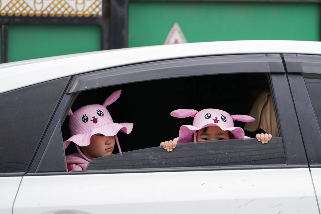 Children wearing hats with cartoon faces wait in a car outside a polling station in a ger district on the outskirts of Ulaanbaatar, Mongolia, Friday, June 28, 2024. Voters in Mongolia are electing a new parliament on Friday in their landlocked democracy that is squeezed between China and Russia, two much larger authoritarian states (AP Photo/Ng Han Guan)