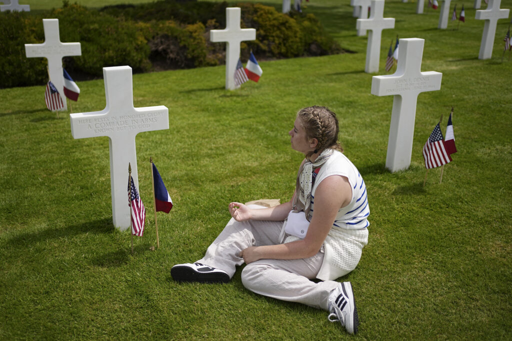 A woman sits by crosses and flags at a US cemetery near Colleville-sur-Mer Normandy, Thursday, June 6, 2024. World War II veterans from across the United States as well as Britain and Canada are in Normandy this week to mark 80 years since the D-Day landings that helped lead to Hitler's defeat. (AP Photo/Laurent Cipriani)