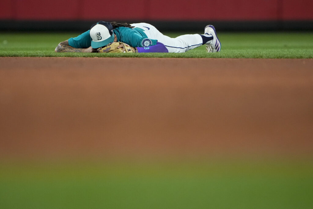 Seattle Mariners shortstop J.P. Crawford lies on the ground after being unable to make the full throw to first base on a single by Minnesota Twins' Carlos Santana during the eighth inning of a baseball game Saturday, June 29, 2024, in Seattle. (AP Photo/Lindsey Wasson)