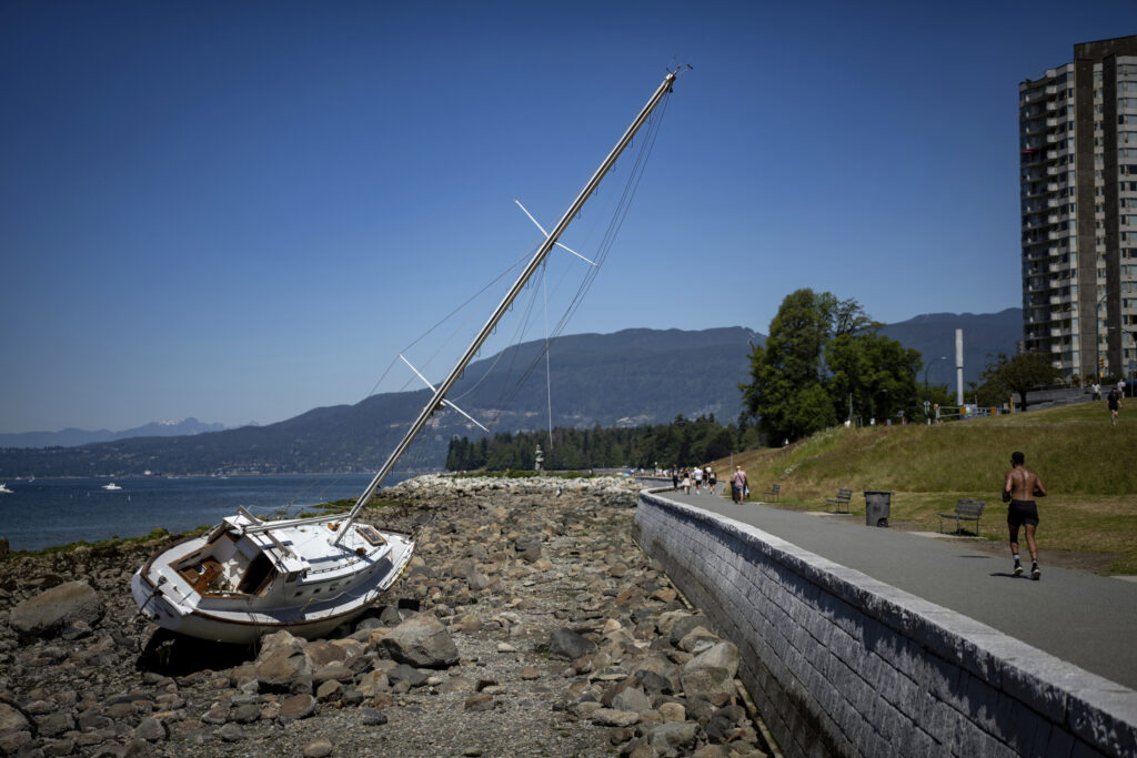 A runner jogs past a beached boat in Vancouver, British Columbia, Sunday, July 7, 2024. Heat warnings have been put in place for the Metro Vancouver area for elevated temperatures. (Ethan Cairns/The Canadian Press via AP)