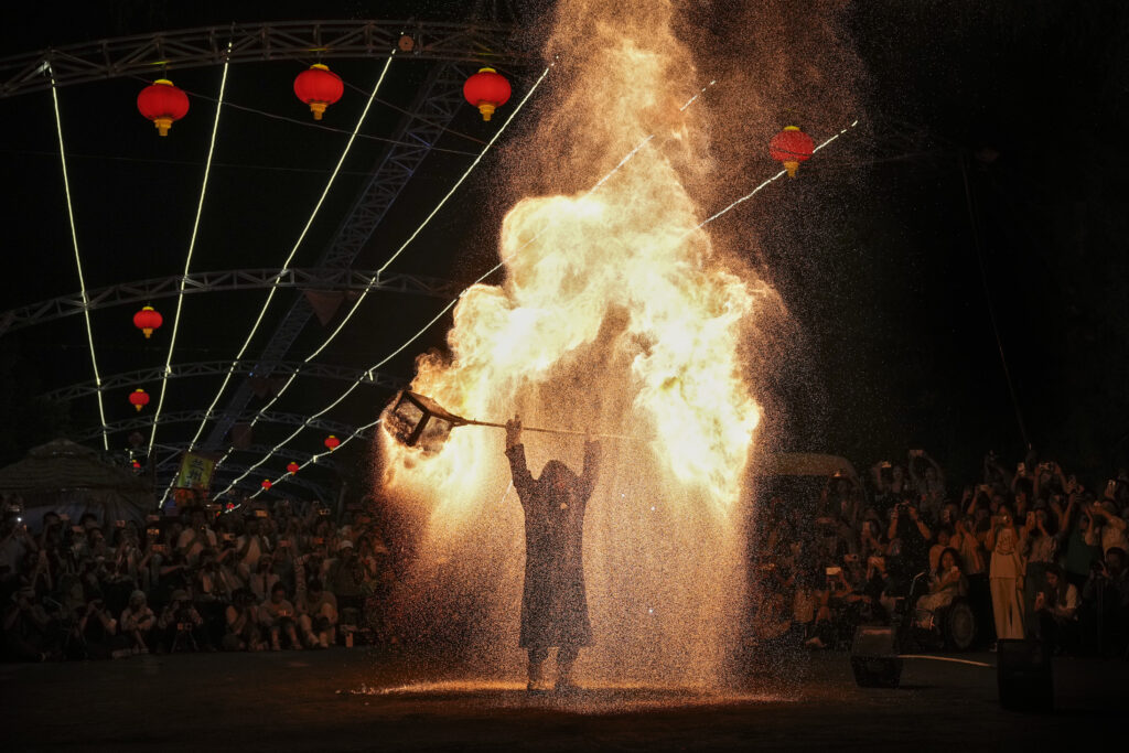 People watch an artist performs a fire kettle show during the Mid-Autumn Festival at a night market in Beijing, Tuesday, Sept. 17, 2024. (AP Photo/Andy Wong)