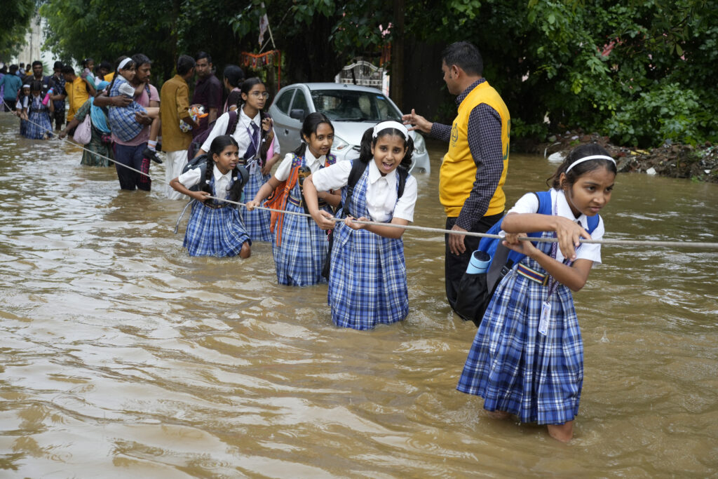 Students hold on to a rope as they cross a street flooded after heavy rains, on their way home in Ajmer, India, Friday, Sept. 6, 2024. (AP Photo/Deepak Sharma)