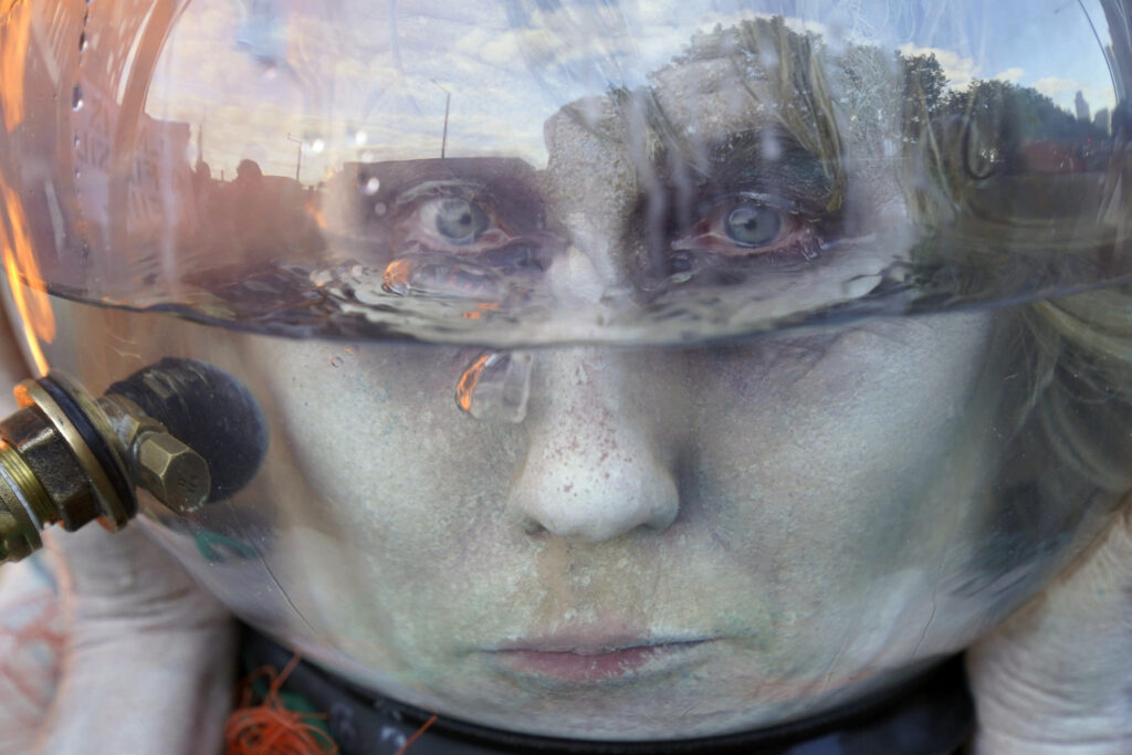 An Ocean Rebellion campaigner, dressed as an oceanic goddess with her head trapped inside a fishbowl-like helmet, takes part in a performance protest outside the International Maritime Organization (IMO) in London, on the final day of the Marine Environment Protection Committee (MEPC) meetings, Friday, Oct. 4, 2024. (Jonathan Brady/PA via AP)