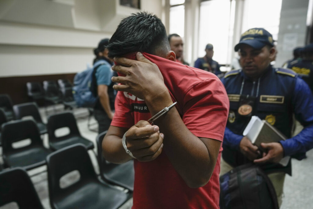 A detained police officer covers his face after a court hearing in Guatemala City, Tuesday, Oct. 1, 2024. Police and alleged human smugglers were arrested Tuesday on migrant extortion charges, according to the Interior Ministry. (AP Photo/Moises Castillo)