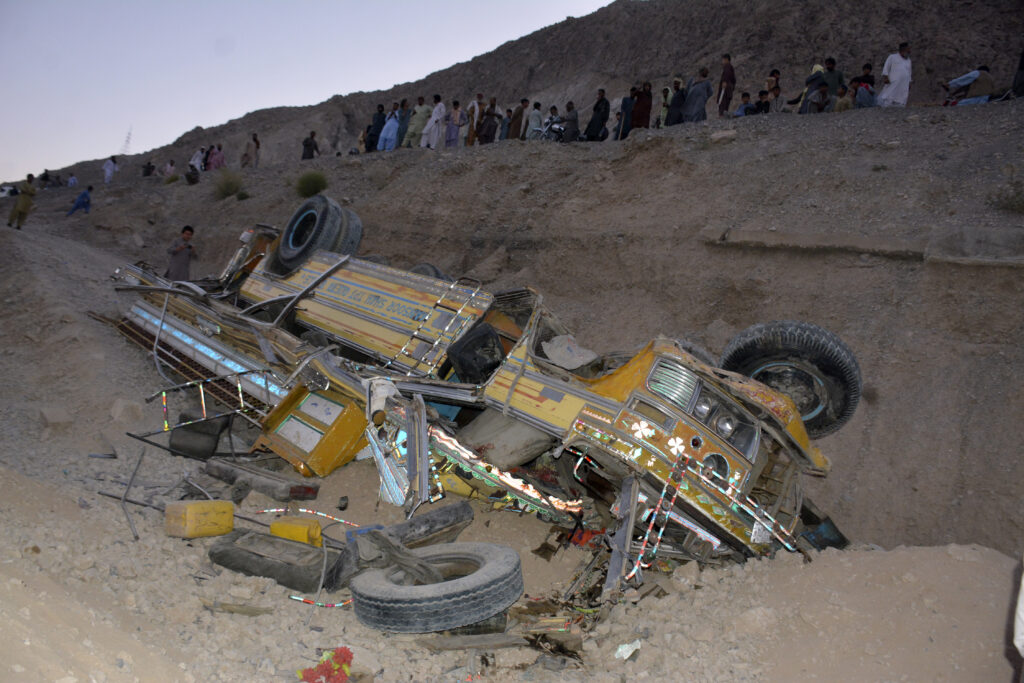 Locals gather near the wreckage of a bus that fell into a ravine near Quetta, the capital of Balochistan province, Pakistan, Thursday, Oct. 3, 2024. A speeding bus carrying wedding guests plunged into a ravine in southwestern Pakistan on Thursday, killing at least seven people, officials and rescuers said. (AP Photo/Arshad Butt)