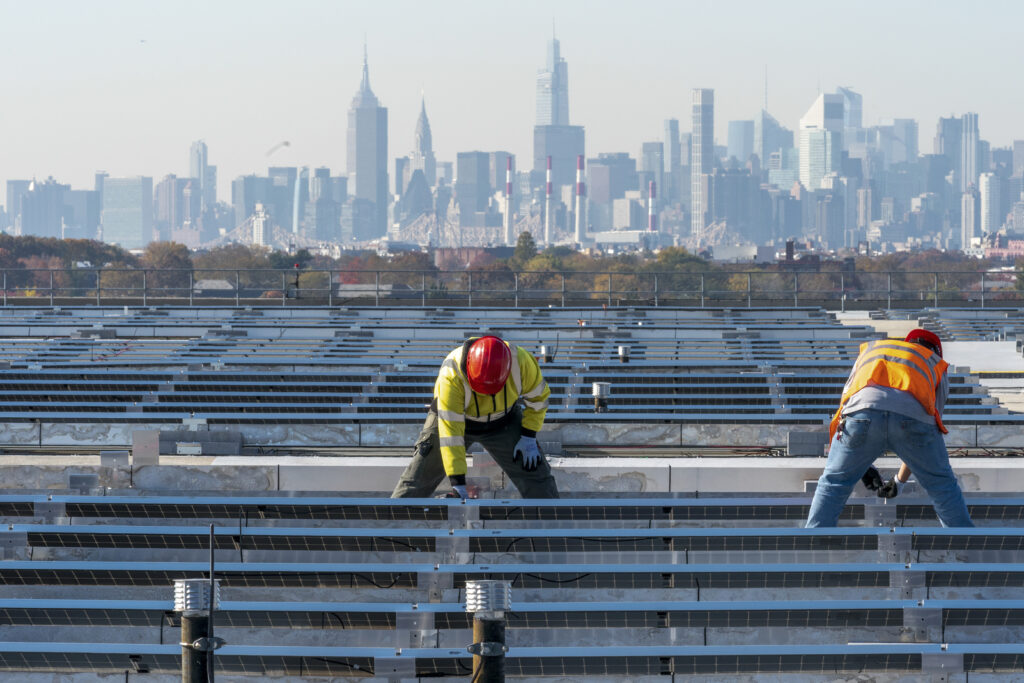 Framed by the Manhattan skyline, electricians with IBEW Local 3 install solar panels. Photo: Mary Altaffer/AP