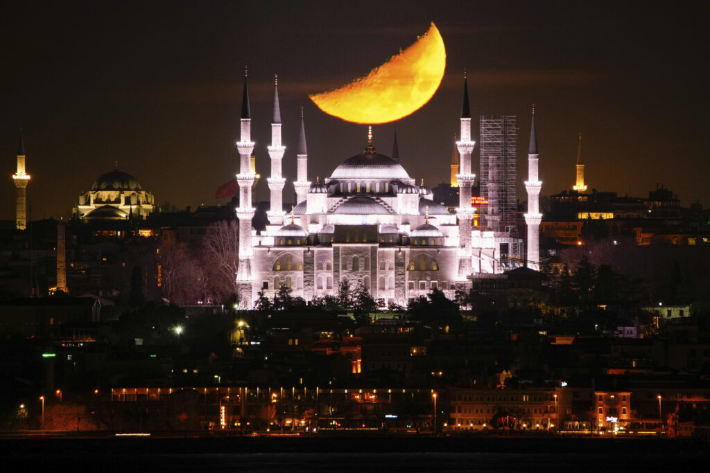 A half-moon sets behind the Sultanahmet Mosque during the Islamic holy month of Ramadan in Istanbul, Turkey, Thursday, March 6, 2025.