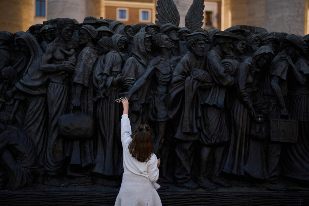 A girl touches the "Angels Unaware" boat sculpture by Canadian artist Timothy P. Schmalz placed at St. Peter's square in Rome, Friday, March 7, 2025.