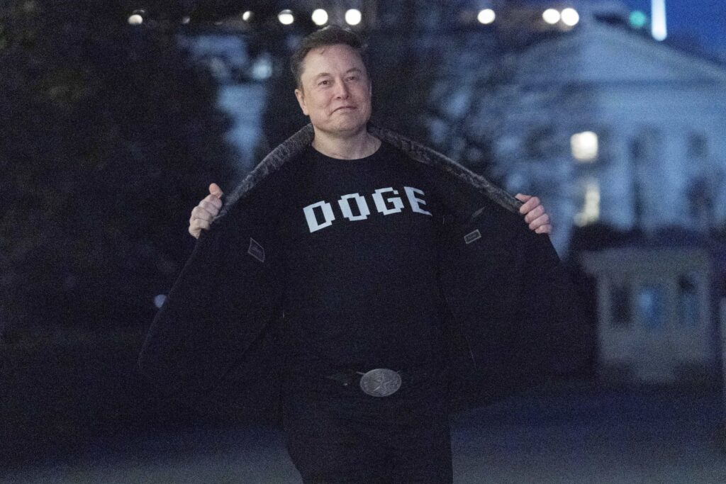 Elon Musk flashes his t-shirt that reads "DOGE" to the media as he walks on South Lawn of the White House, in Washington, Sunday, March 9, 2025.