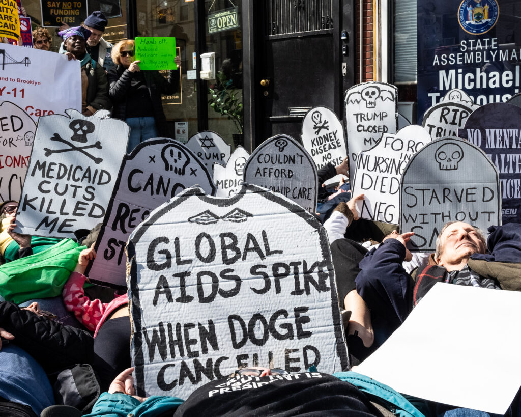 A coalition of progressive organizations and unions — including Indivisible Brooklyn and 1199 SEIU United Healthcare Workers East — stage a die-in outside the Bay Ridge office of Congresswoman Nicole Malliotakis (R-Brooklyn), in Brooklyn, New York, on March 22, 2025, protesting her vote to cut funding for federal health care programs and give tax breaks to billionaires. Brooklyn Eagle photo by Gabriele Holtermann