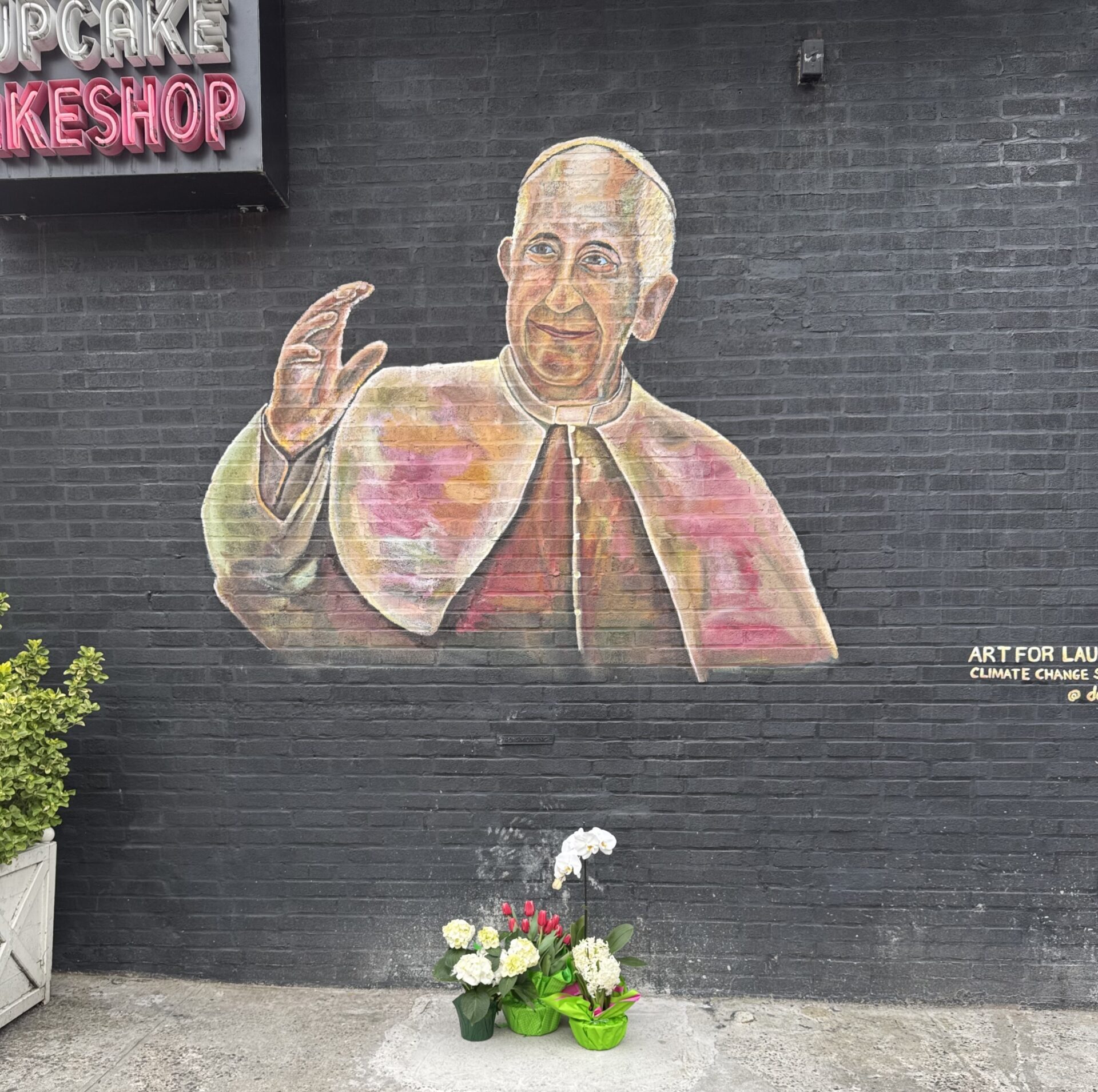 The mural of Pope Francis in Bay Ridge now has flowers underneath it. Photo courtesy of Delphinoto