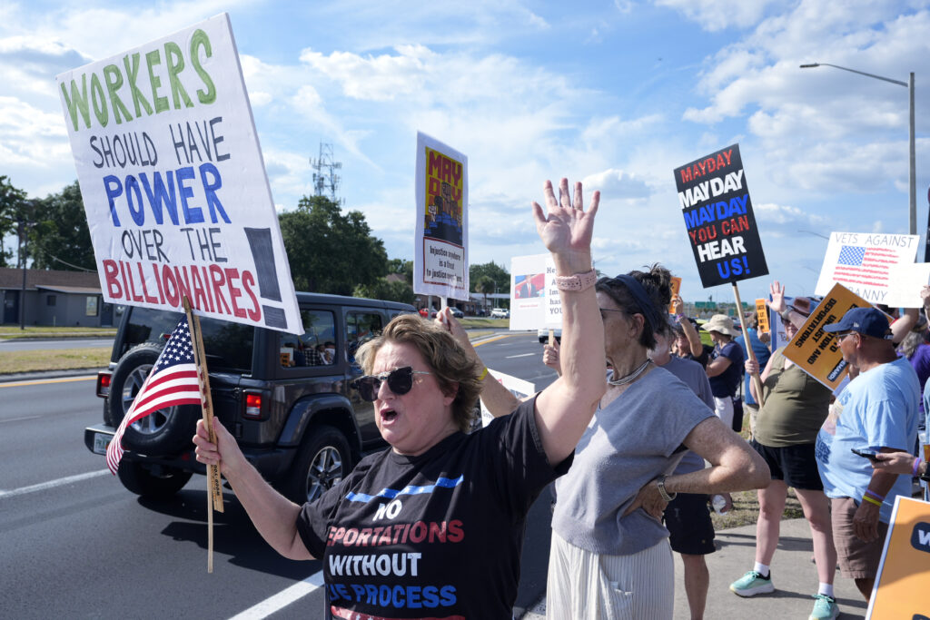 Demonstrators hold signs and wave to motorists in front of the Orange County Corrections Department during a May Day rally for worker and immigrant rights Thursday, May 1, 2025, in Orlando, Fla.