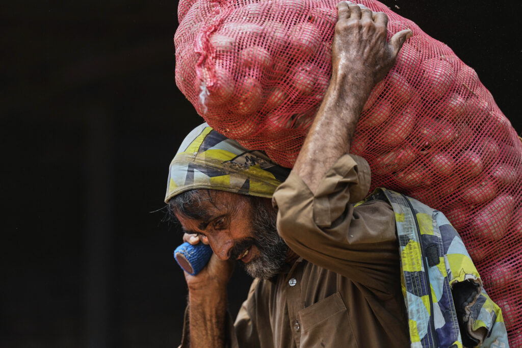 A laborer carries a sack of potatoes to load it into a mini truck at a wholesale vegetable market, during May Day in Islamabad, Pakistan, Thursday, May 1, 2025.