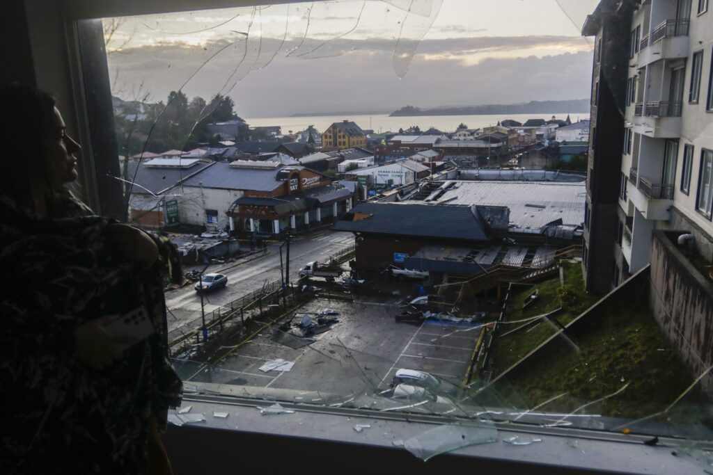 A woman looks through her home's broken window at more damage the day after tornado hit Puerto Varas, Chile, Monday, May 26, 2025.
