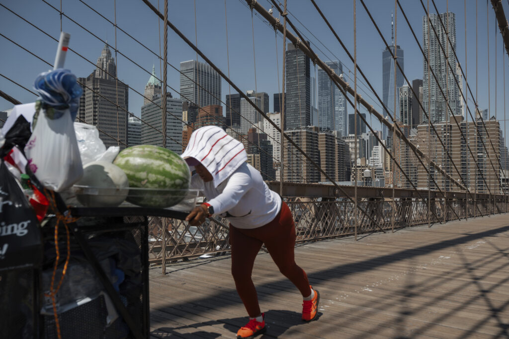 A fruit vendor pushes her cart on the Brooklyn Bridge during a heat wave on Tuesday, June 24, 2025, in New York.