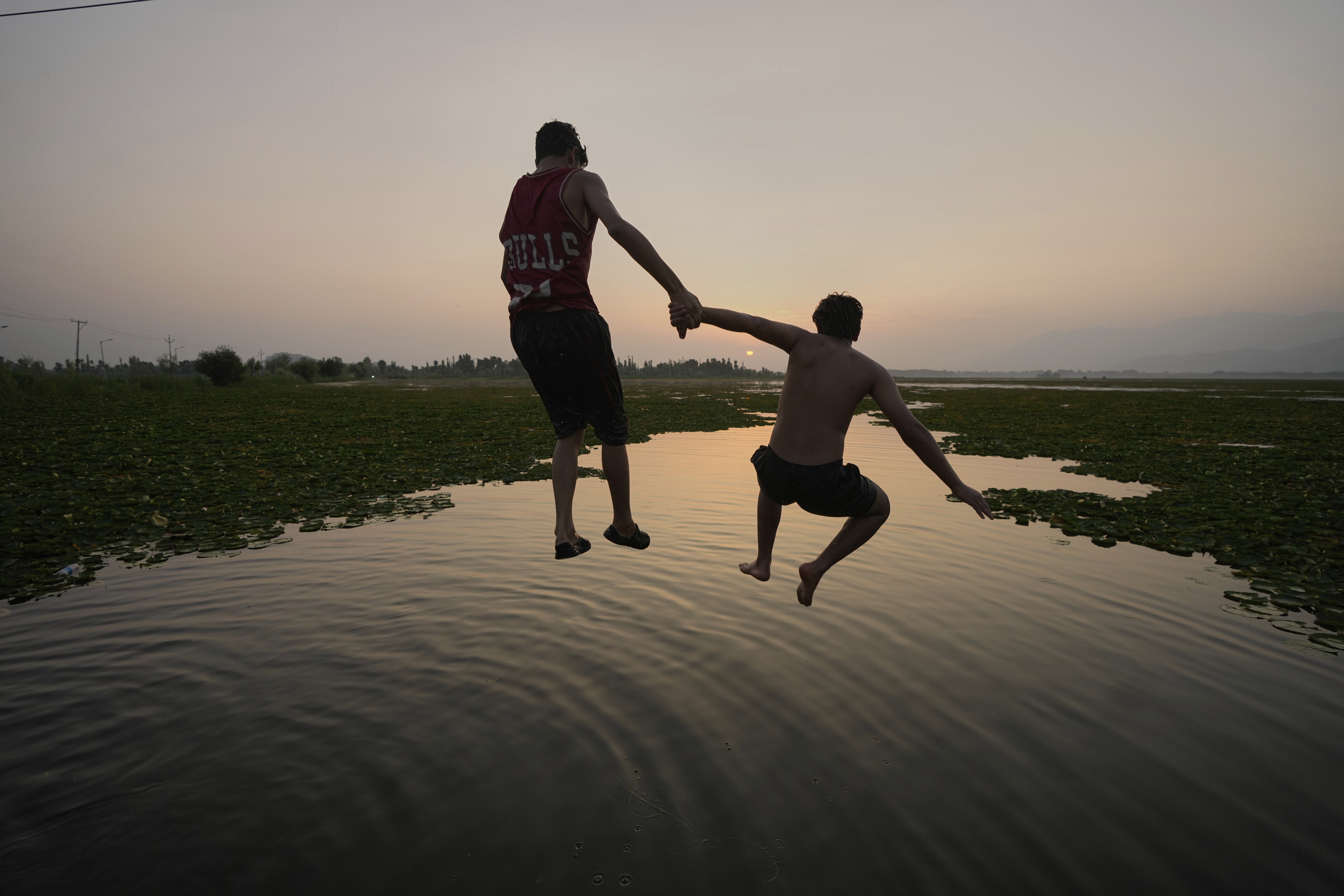 Boys jump together as they cool off on a hot summer day at Dal Lake in Srinagar, Indian-controlled Kashmir, Monday, June 23, 2025.