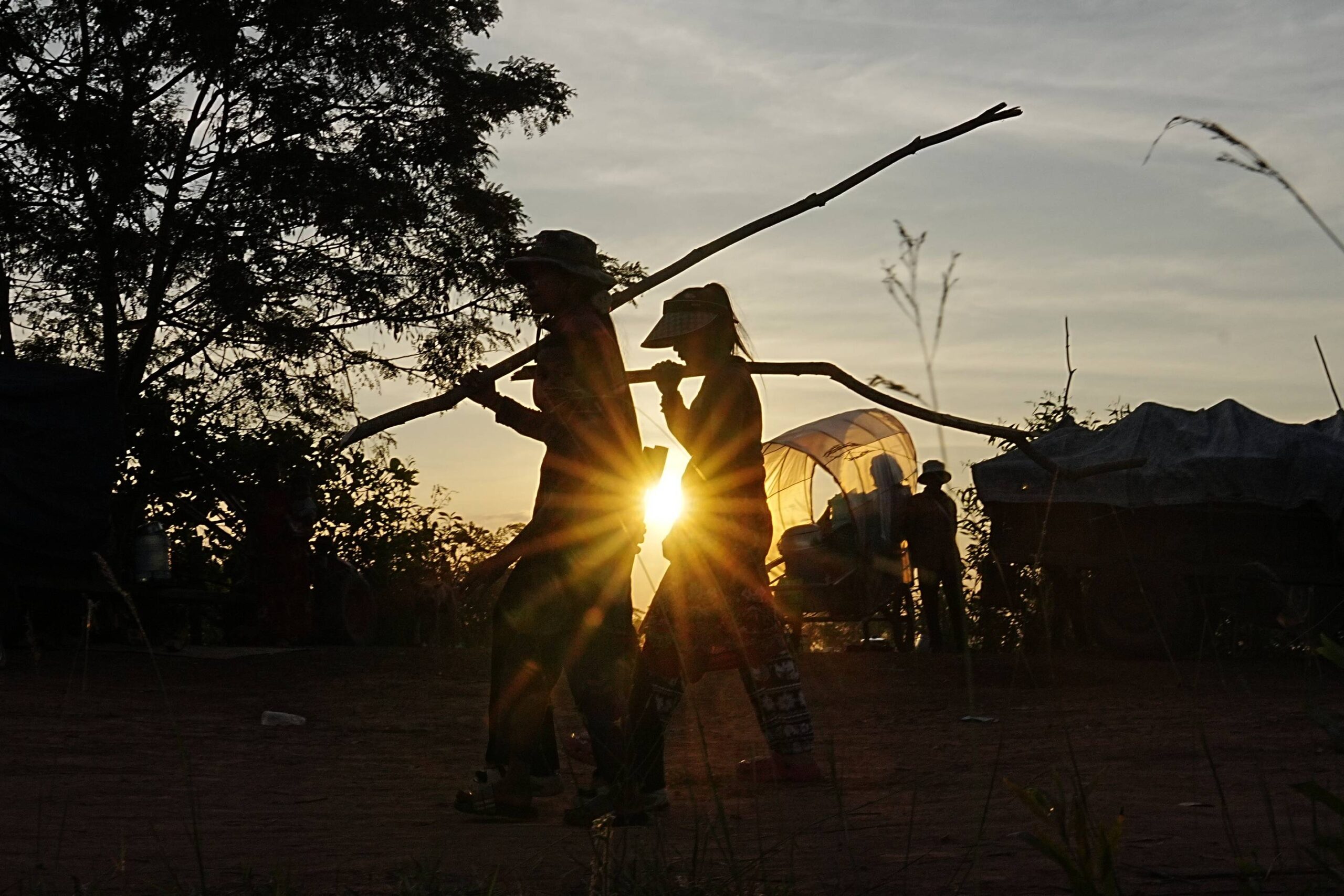 Local people are silhouetted as they carry wooden sticks to make a shelter in Srey Snam, Siem Reap province after fleeing home at Cambodia's border with Thailand, Tuesday, Dec. 9, 2025. Photo: Heng Sinith/AP