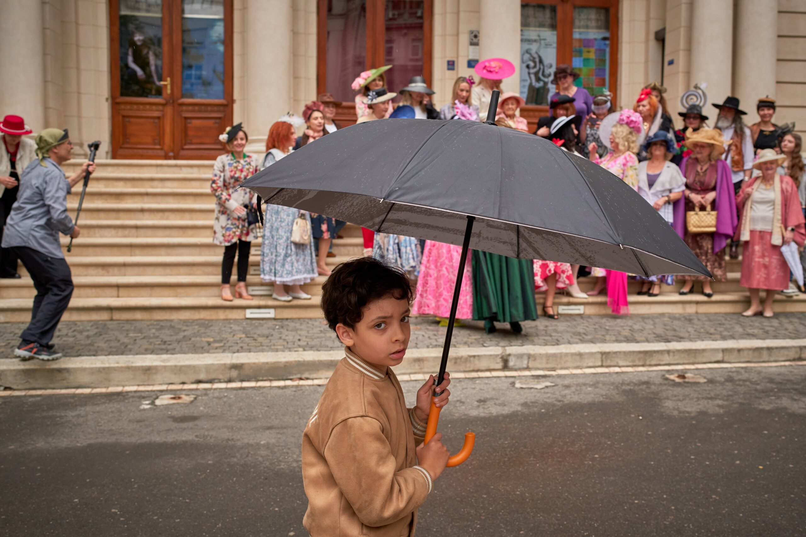 A child holds an umbrella as participants in the World Hat Walk, an event which, according to organizers, takes place in up to 60 cities across the world, promoting headwear, pose for pictures in Bucharest, Romania, Sunday, May 10, 2026. Photo: Vadim Ghirda/AP