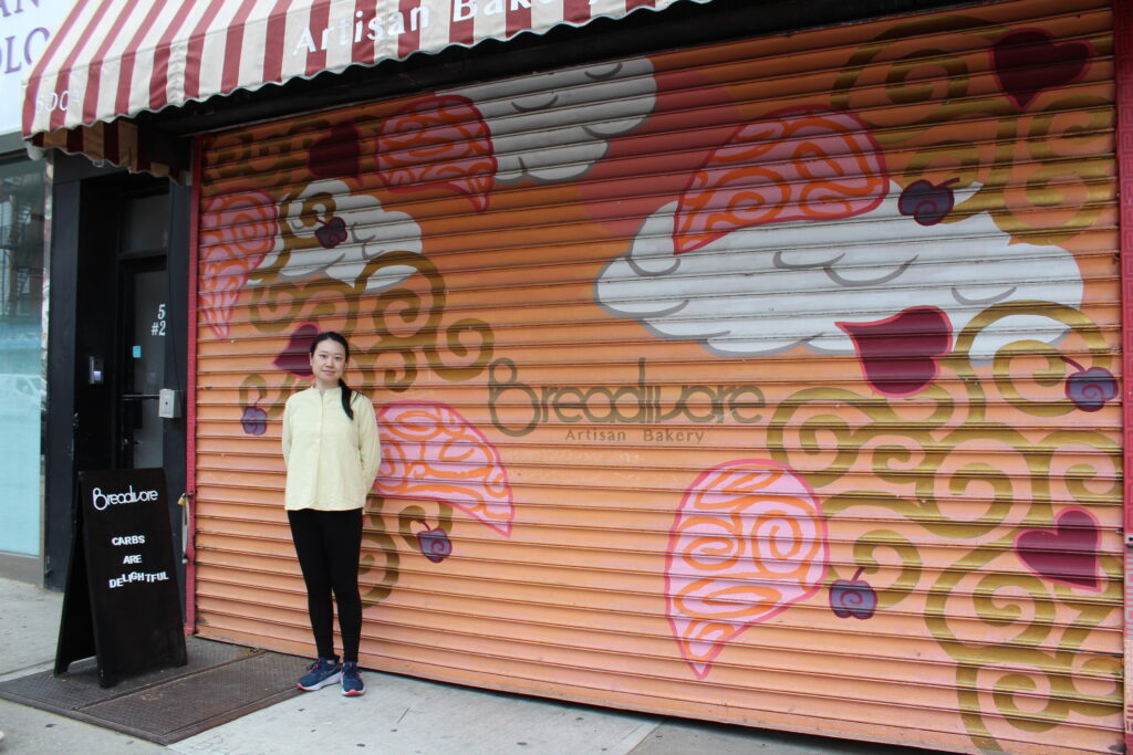 Cixiu Gao, owner of Breadivore, stands in front of her gate with a mural painted by John Horowitz. Photo: Allegra Acevedo