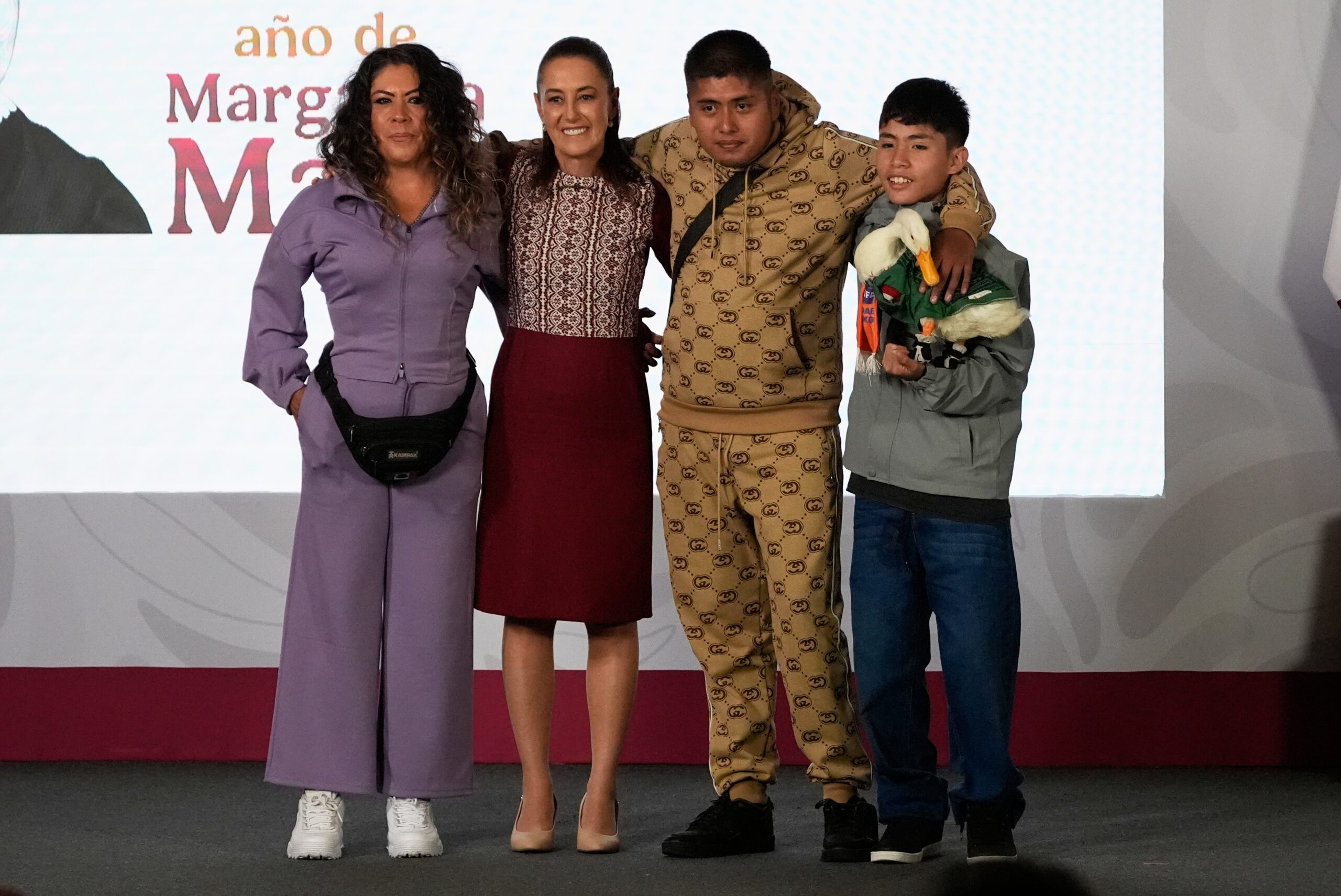 Merlin the duck, dressed in a Mexican national soccer team jersey, attends the daily press conference by Mexican President Claudia Sheinbaum, second from left, along with his caretakers Carla Gomez and her sons Carlos, and Christian who holds Merlin, at the National Palace in Mexico City, Monday, June 22, 2026. Photo: Marco Ugarte/AP