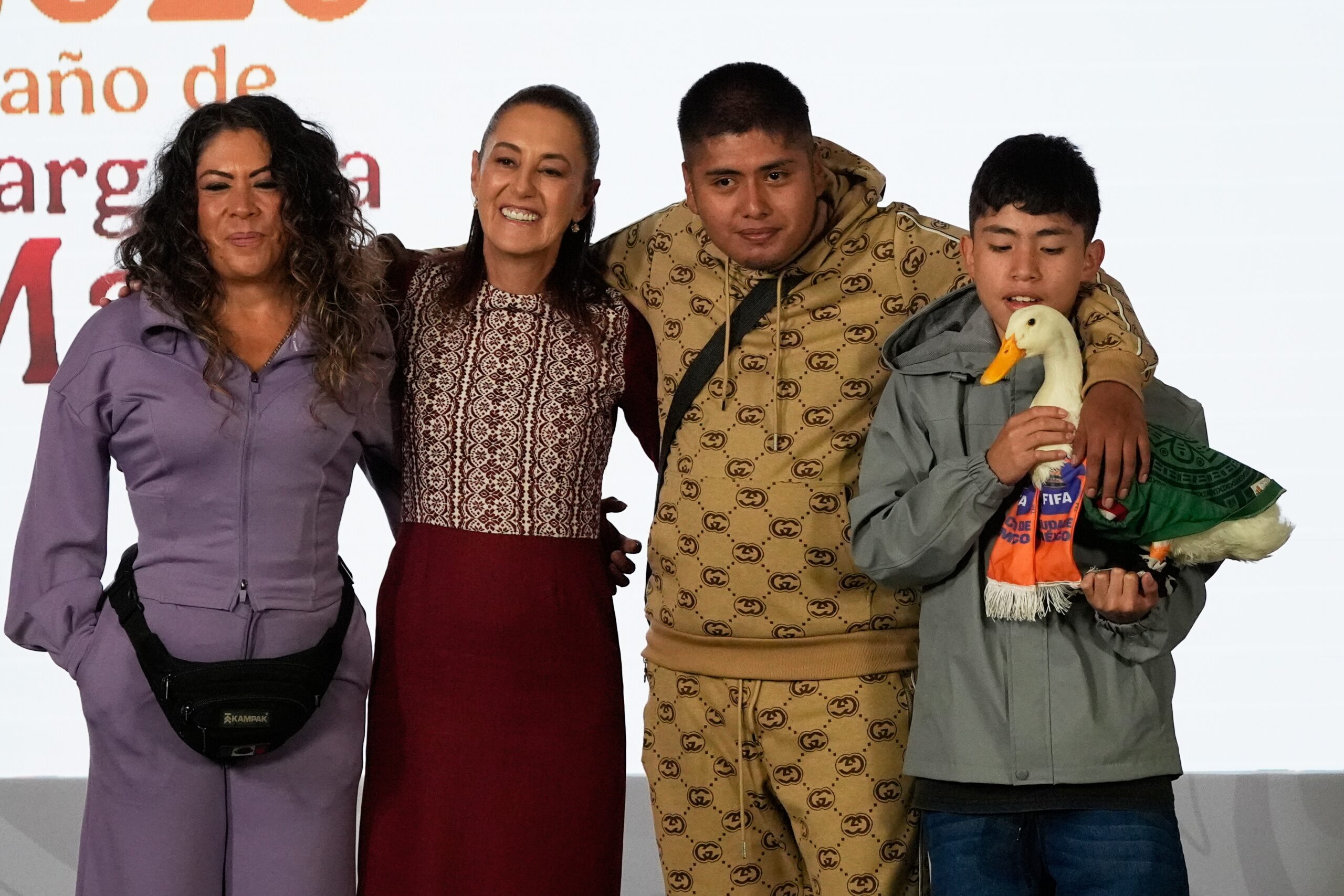 Merlin the duck, dressed in a Mexican national soccer team jersey, attends the daily press conference by Mexican President Claudia Sheinbaum, second from left, along with his caretakers Carla Gomez and her sons Carlos, and Christian who holds Merlin, at the National Palace in Mexico City, Monday, June 22, 2026. Photo: Marco Ugarte/AP