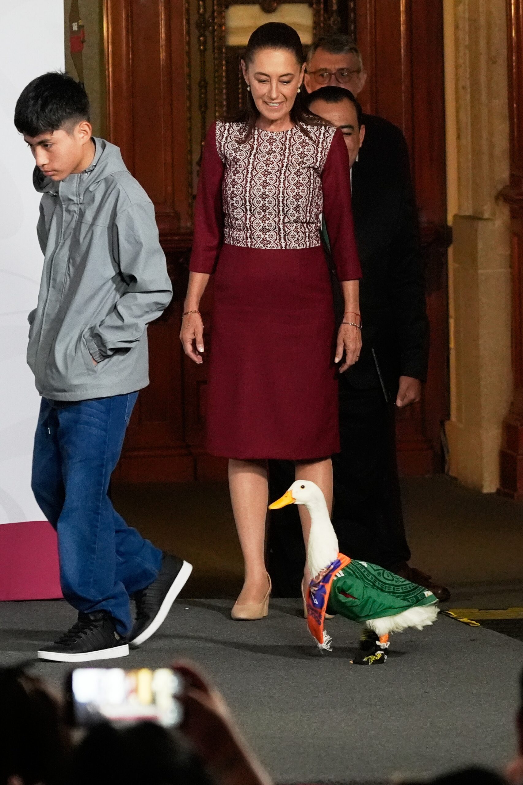 Merlin the duck, dressed in a Mexican national soccer team jersey, arrives for the daily press conference by Mexican President Claudia Sheinbaum, along with the duck's caretaker Christian Gomez, left, at the National Palace in Mexico City, Monday, June 22, 2026. Photo: Marco Ugarte/AP