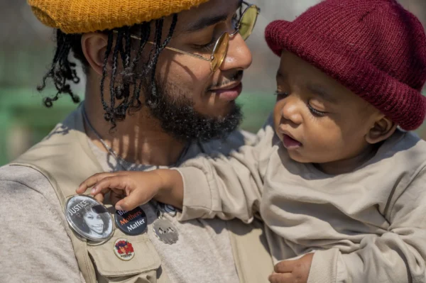 Bruce McIntyre holds his son, Elias, as the young boy reaches for a button depicting his mother that reads “Justice For Amber.” Credit: Hiram Alejandro Durán/The City Reporter