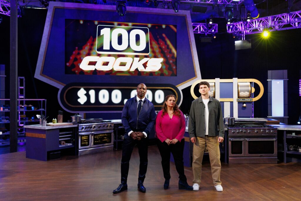 Host Terry Crews with Judges Alex Guarnaschelli and Nick DiGiovanni posed in front of LED board, as seen on 100 Cooks, Season 1.