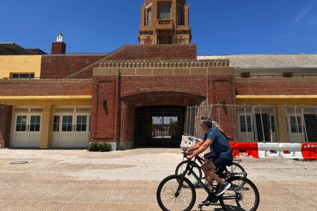 Boardwalk bikers pass the under-construction Rockaway Ocean Club, July 20, 2026. Credit: Kaitlyn Schwanemann/The City Reporter
