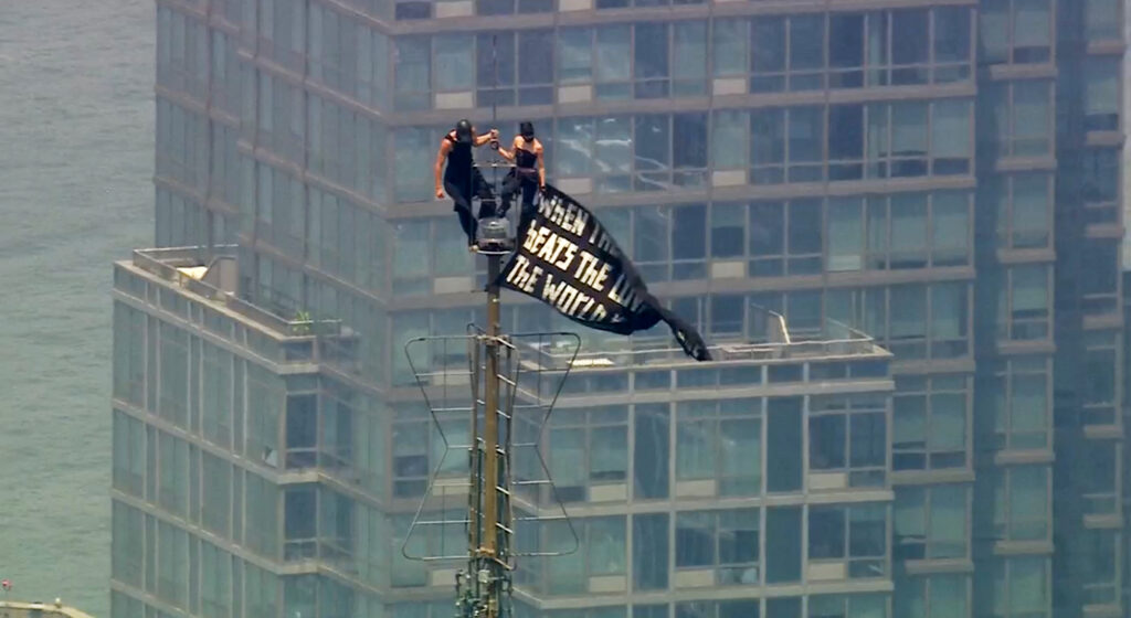 Two people stand on the tip of the antenna of the Empire State Building in New York while holding a banner on Wednesday, July 1, 2026. Photo: WABC-TV via AP
