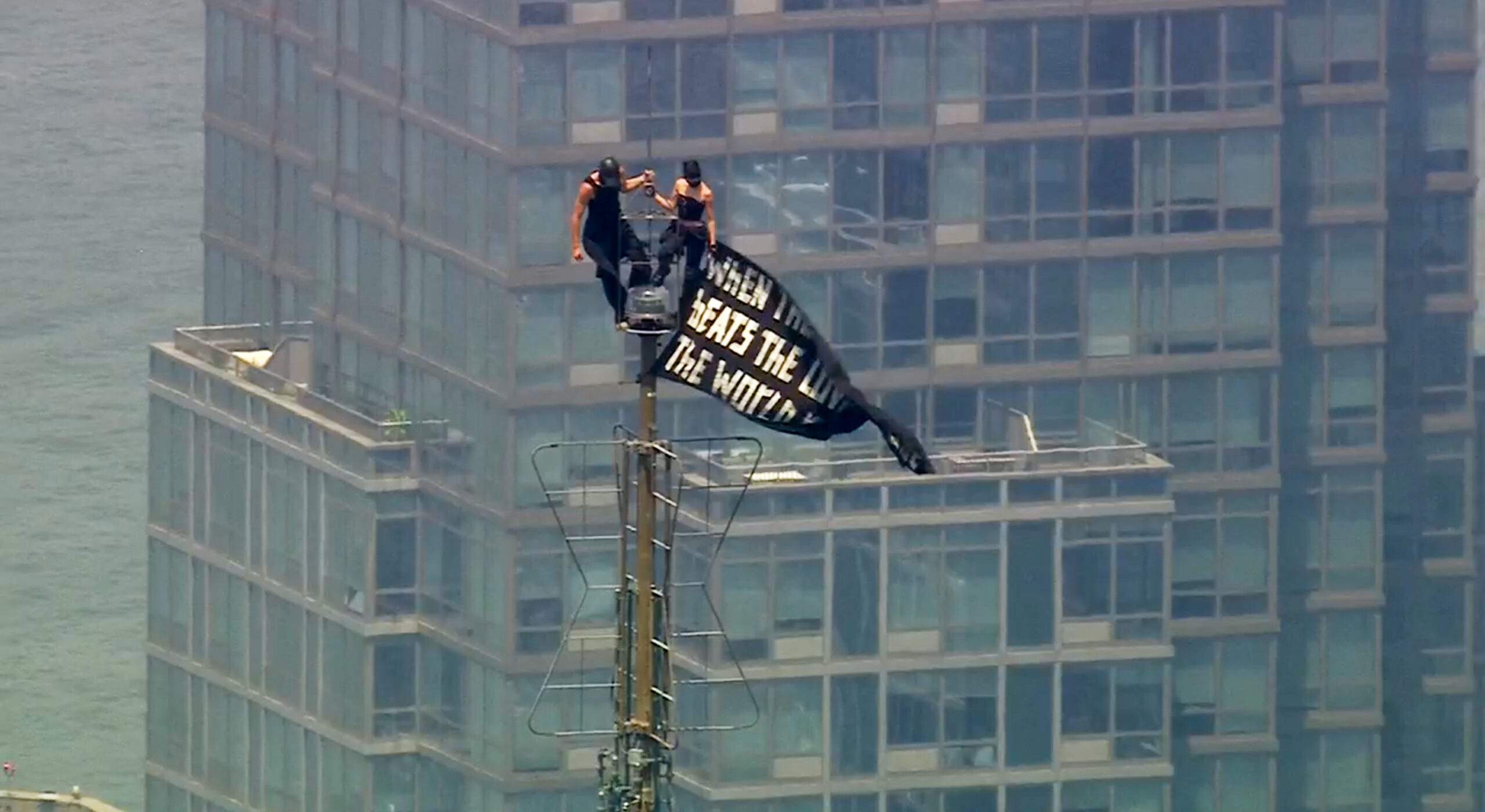 Two people stand on the tip of the antenna of the Empire State Building in New York while holding a banner on Wednesday, July 1, 2026. Photo: WABC-TV via AP