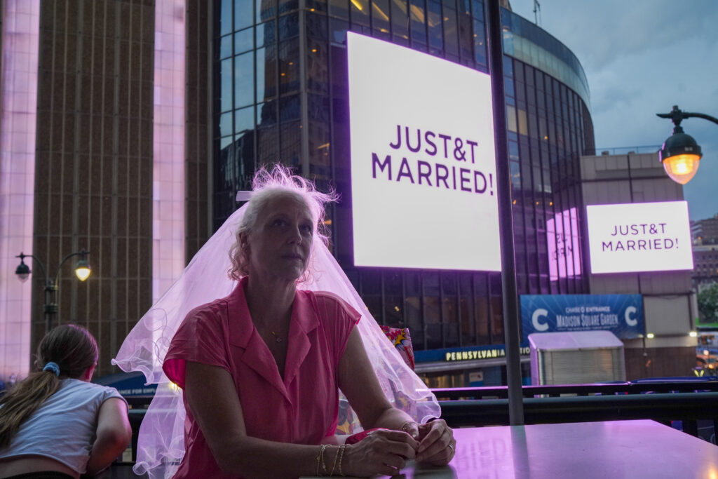 A Taylor Swift fan wearing a wedding veil sits at a restaurant next to Madison Square Garden where a "JUST&T MARRIED" sign is displayed during a wedding between singer Taylor Swift and National Football League player Travis Kelce on Friday, July 3, 2026, in New York. Photo: Ryan Murphy/AP